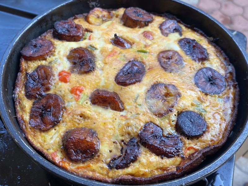 Egg and plantain frittata with golden fried plantain slices on top, cooking in a pan